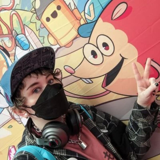 Jay is posing at a gaming convention, looking at the camera and making a peace sign.